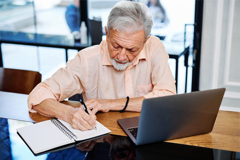 Senior man writes notes next to his laptop