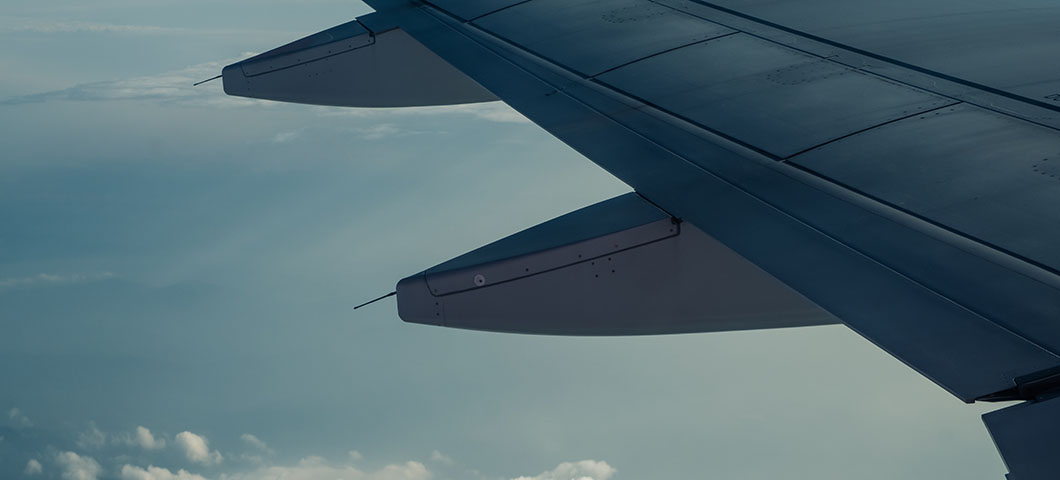An airplane wing through airplane window with a cloudy sky background